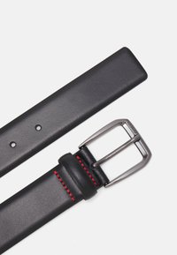 Ceinture en cuir noir avec une texture lisse, boucle en métal argenté et détails de couture rouge près de la boucle. Dispose de trous pour réglage.
