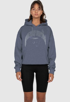 Grauer Kapuzenpullover mit grafischem Druck, in lockerer Passform und mit gerippten Bündchen, kombiniert mit schwarzen Shorts. Glatte Stofftextur.