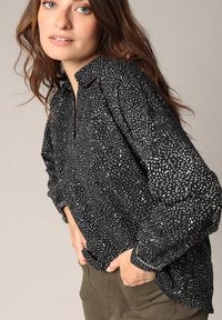 Zwarte blouse met wit gespikkeld patroon, kraaghalslijn en lange mouwen. Zachte stof met lichte glans, relaxte pasvorm en verlaagde schouders.