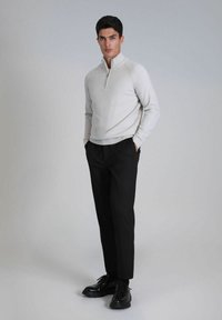 Hellgrauer Quarter-Zip-Pullover mit langen Ärmeln, kombiniert mit schwarzen, maßgeschneiderten Hosen und schwarzen Schnürschuhen. Glatte Textur und körperbetontes Design.