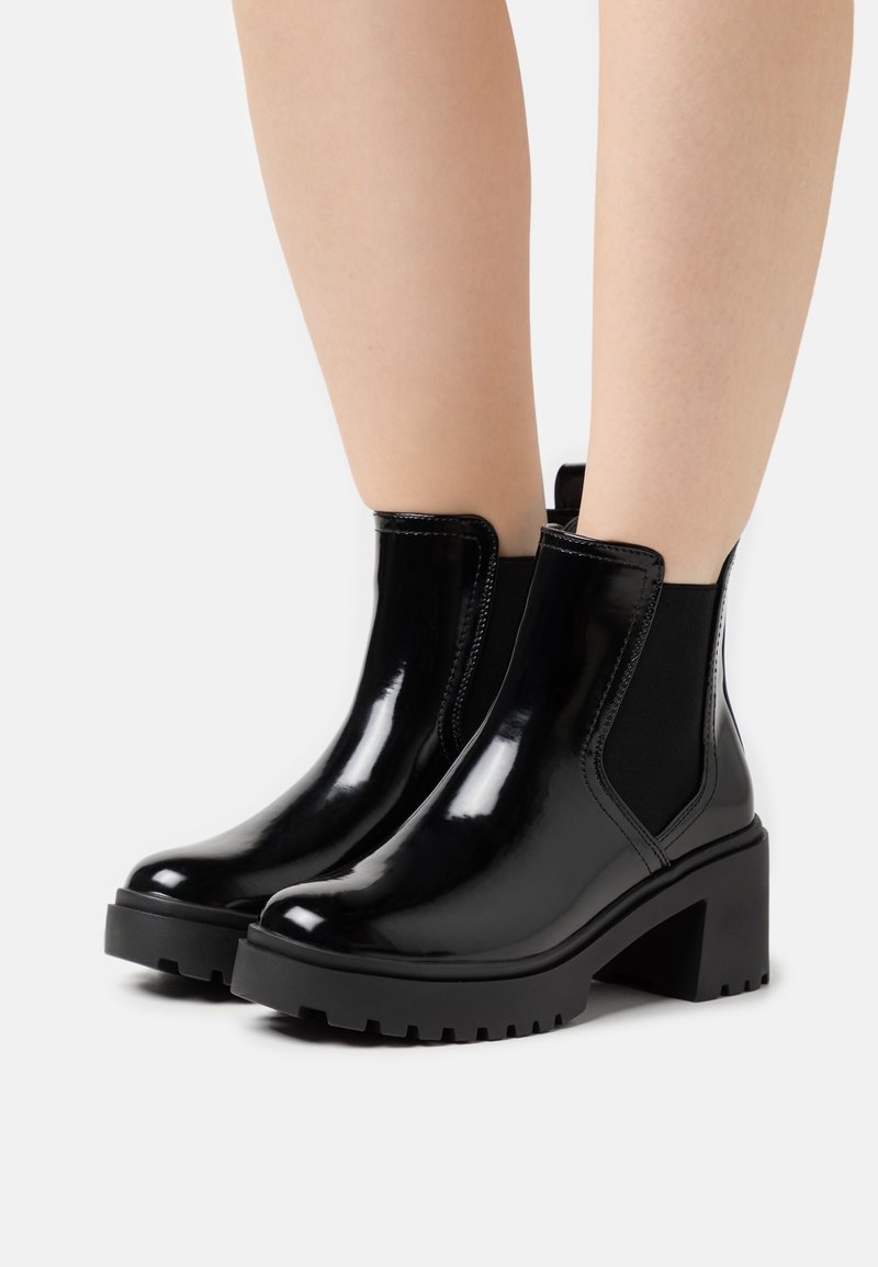 Botines negros de charol con paneles laterales elásticos y un tacón grueso, que cuentan con una suela de goma texturizada para mayor tracción.