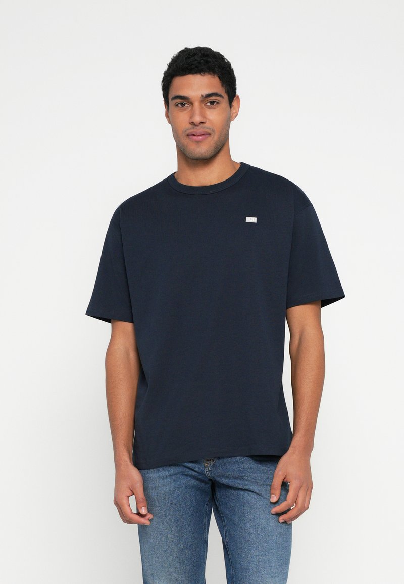 Μπλε ναυτικό βαμβακερό t-shirt με κοντά μανίκια, στρογγυλή λαιμόκοψη και μικρή λεπτομέρεια λογότυπου στο στήθος. Ομαλή υφή, άνετη εφαρμογή.