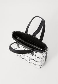 Sac fourre-tout avec un extérieur en noir et blanc texturé, doté de poignées en cuir, d'une poche intérieure zippée et d'une forme rectangulaire structurée.