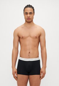 Boxer shorts noirs avec une ceinture grise arborant le logo "COPENHAGEN STUDIOS", fabriqués en tissu extensible, design ajusté, texture lisse.