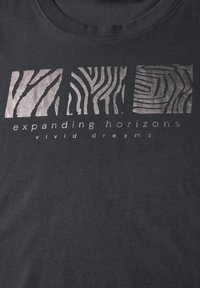 Svart bomull T-shirt med metalliskt silverfärgade zebramönster och texten "utvidgande horisonter livliga drömmar" nedanför.