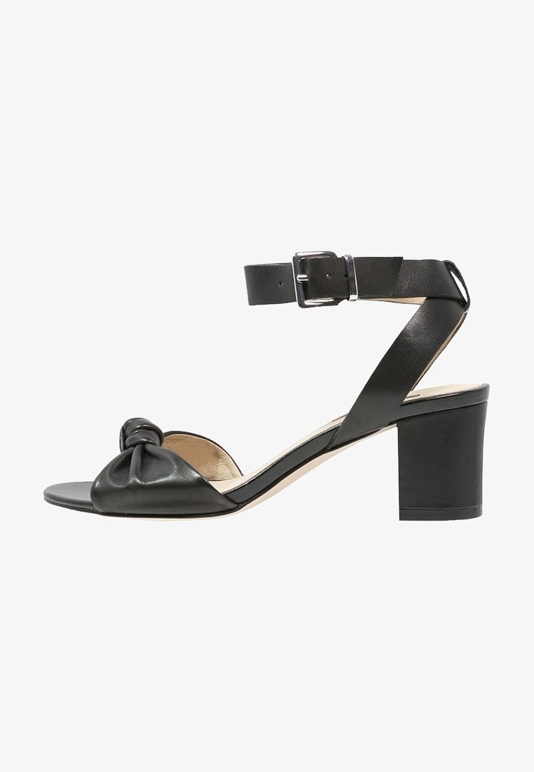 Sandale noire en cuir à bout ouvert, talon bloc, bride avant nouée, et bride de cheville réglable avec boucle argentée.