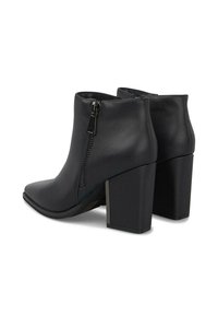 Botas de cuero negras hasta el tobillo con tacones cuadrados, cremalleras laterales y punteras afiladas, mostradas desde un ángulo trasero en tres cuartas partes.
