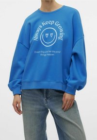 Sudadera azul con cuello redondo, mangas oversize y estampado de texto gráfico blanco y cara sonriente. Material suave de mezcla de algodón.