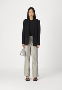 Black blazer over a black top, metallic silver textured pants, black sandals with gold accents, and a small silver handbag.