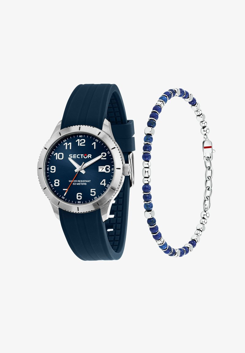Orologio con cinturino in silicone blu, cassa in acciaio inossidabile con finitura argentata, indicatori delle ore bianchi, oblò per la data; affiancato da un bracciale di perline blu con dettagli argentati.