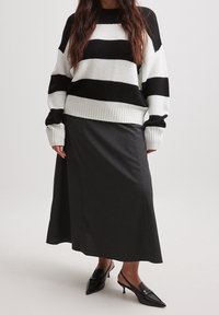 Zwart-wit gestreepte gebreide trui met een geribde zoom, gecombineerd met een donkergrijze rok. Zwarte puntige slingback hakken maken de outfit compleet.