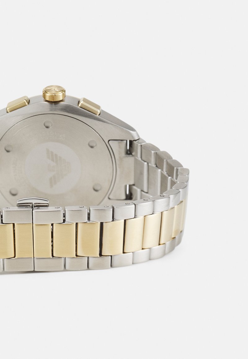 Edelstahlarmbanduhr mit einem silbernen und goldfarbenen Metallband. Rundes Gehäuse mit einer goldenen Krone und zwei goldenen Knöpfen. Gravierter Rücken.