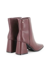 Par de botas de tobillo en malva oscuro con tacones de bloque, cremalleras laterales y pequeños acentos metálicos en la parte superior y la suela.