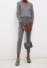 Persona che indossa un maglione grigio lavorato a maglia e pantaloni grigi aderenti, con una piccola borsa a tracolla in stampa pelle di serpente e indossa stivaletti grigi in suede.