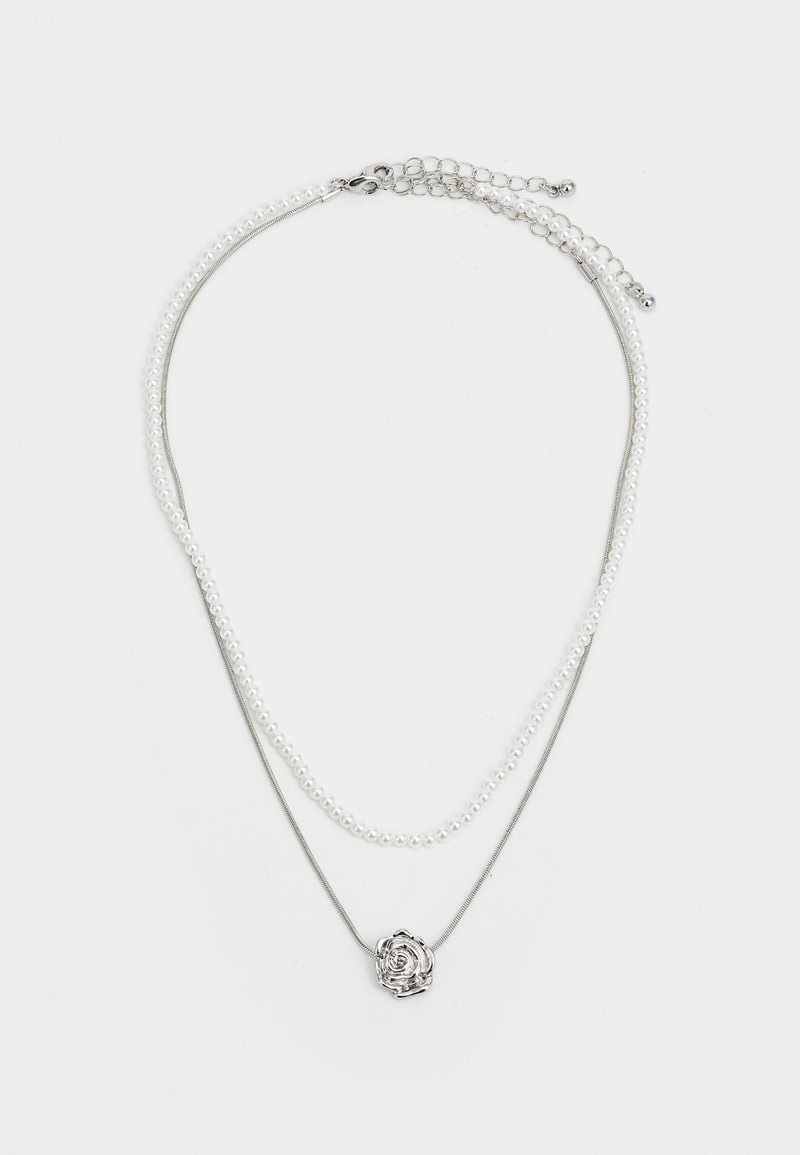 Mehrschichtige Halskette mit einer silbernen Kette und einer Perlenstrang. Im Mittelpunkt steht ein rosenförmiger Anhänger, der Details hinzufügt. Glatte Textur und metallischer Glanz.