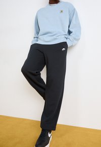 Ljusblå sweatshirt med en logotyp, tillsammans med svarta sweatpants med en vit Nike-logotyp. Svarta sneakers med vita detaljer.