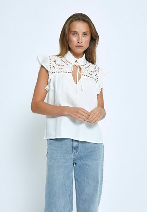White blouse with lace detailing, ruffled sleeves, and a tie-neck design. Paired with light blue denim, displayed against a plain background.