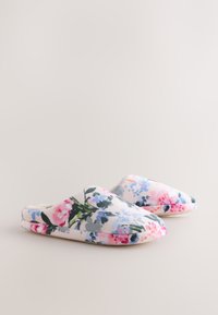 Pehmead slip-on tüüpi sussid roosa, sinise ja rohelise lillemustriga heledal taustal, näidatud neutraalse tasase pinna taustal.
