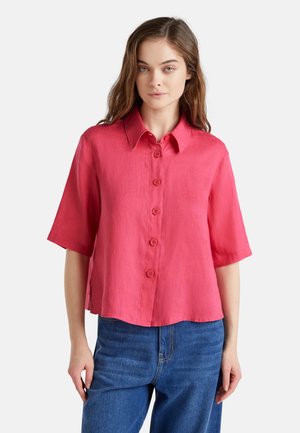 Rosa Leinen-Hemdkurzarmshirt mit Knopfleiste, Kragen und lockerer Passform. Kombiniert mit hochgeschnittenen blauen Jeans.