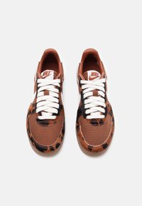 Tenisii Nike cu un model din pânză maro și imprimeu leopard, șireturi albe și un design cu vârf rotunjit, având o suprafață texturată.