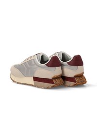 Zapatillas deportivas con parte superior beige y gris, acentos en color marrón, suela de goma texturada y cuellos acolchados. Presenta un acabado suave y un diseño en capas.