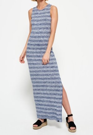 Robe maxi sans manches bleue et blanche à rayures avec fente sur le côté, portée avec des sandales à plateforme noires par une personne debout.