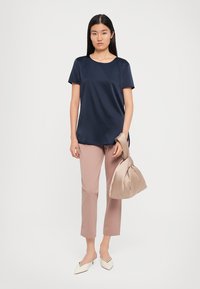 Top corto navy a maniche corte con una vestibilità rilassata, abbinato a pantaloni tapered rosa chiaro, décolleté crema a punta e una borsa in satin beige.