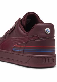 Rote Leder-Sneaker mit einem kastanienbraunen Finish, ausgestattet mit horizontalen blauen und roten Streifen, strukturierten Akzenten und einem Markenlogo auf der Ferse.