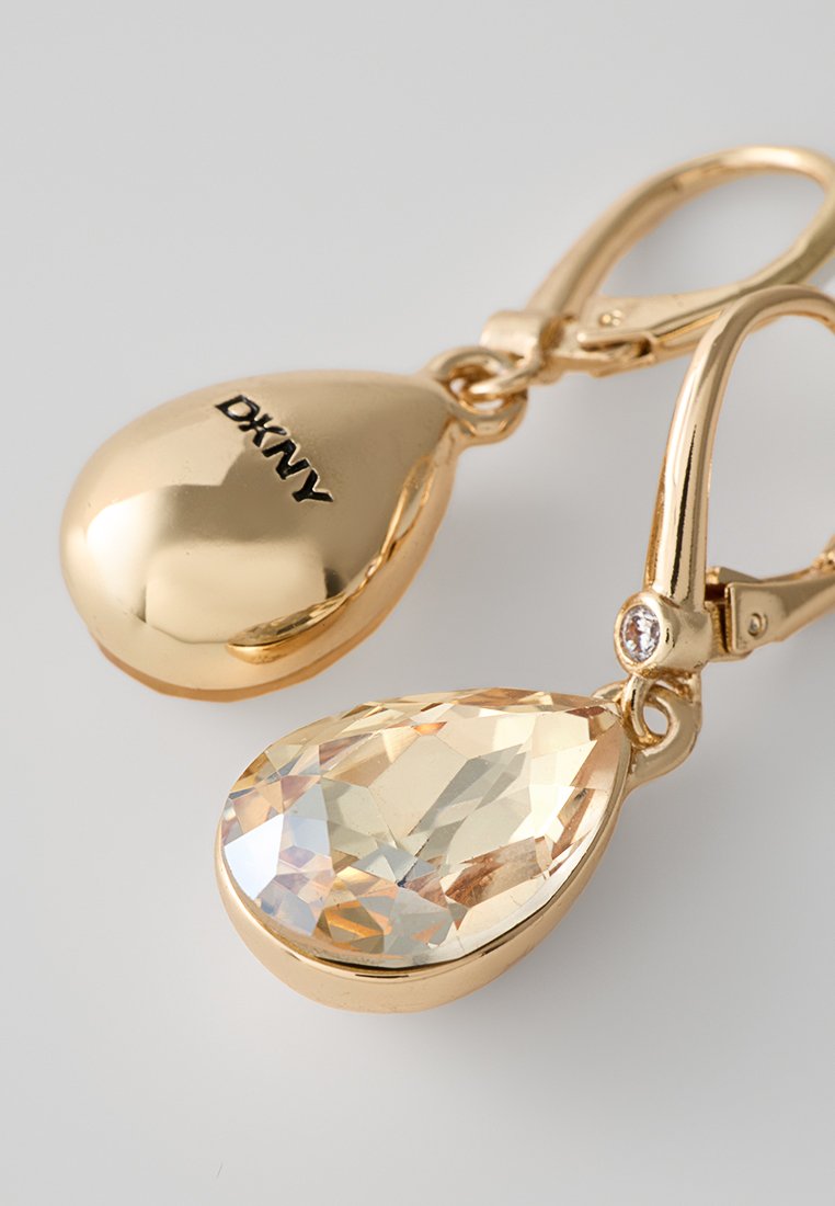 Ohrringe mit Goldton, die mit tropfenförmigen Kristallen in klaren und hellgoldenen Farbtönen verziert sind, welche mit einem Hebelverschluss befestigt sind.