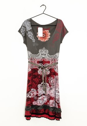 Vestito a maniche corte con top grigio, gonna rossa e nera a fantasia, motivi bianchi simili a pizzo e cintura annodata in vita appesa a una gruccia nera.