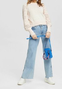 Pull en tricot rose clair avec manches ajourées, associé à un jean large bleu clair. Accessoire compris : un petit sac bandoulière bleu.