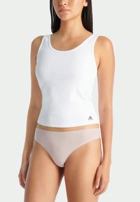 Witte geribbelde tanktop met brede bandjes, met een klein grijs Adidas-logo. Draagt met lichtroze naadloze onderkleding.