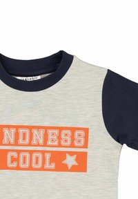 Grå t-shirt med korte ærmer, navy detaljer og orange trykt tekst, der står "KINDNESS COOL", med en stjerne grafik.