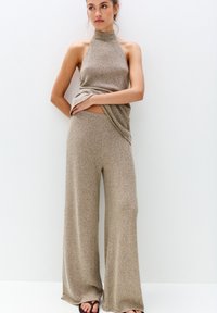 Ensemble en tricot beige composé de deux pièces avec un haut à col haut et un pantalon évasé, mettant en valeur un motif texturé et des éléments de conception drapés.