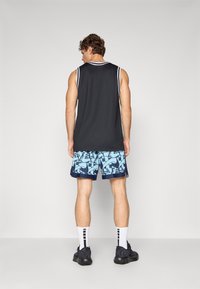 Sleeveless black athletic shirt with white trim, paired with blue patterned shorts featuring geometric designs. Black sports shoes and white socks.