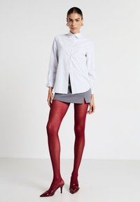 Camicia a righe bianco e grigio chiaro con bottoni, gonna mini grigia con spacco laterale, collant rossi opachi e scarpe col tacco appuntite in vernice bordeaux.