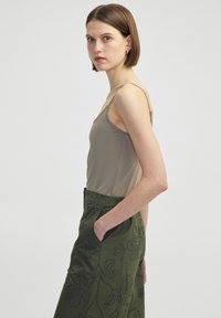 Olivgrünes Trägershirt, kombiniert mit einem gemusterten, grünen Rock mit floralen Details. Das Oberteil hat dünne Träger und ein tailliertes Design.