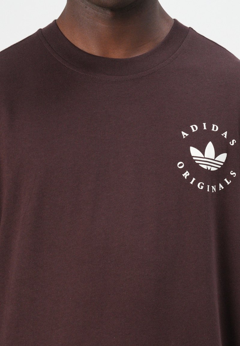 T-shirt di cotone bordeaux scuro con collo a giro, maniche corte e logo Adidas bianco con testo "ORIGINALS" sul lato sinistro del petto.