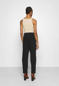 Pantalones negros de cintura alta con un corte relajado, que cuentan con una cinturilla ajustable y dobladillos acampanados, combinados con una camiseta sin mangas de punto beige.