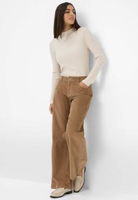 Haut beige à rayures avec des manches longues associé à un pantalon large en velours côtelé marron. Les chaussures sont de couleur blanc cassé avec un design de mocassins et un petit talon bloc.