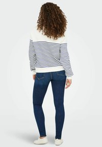 Bawełnowy sweatshirt w niebiesko-białe poziome paski, w połączeniu z ciemnoniebieskimi skinny jeansami. Białe trampki dopełniają strój.