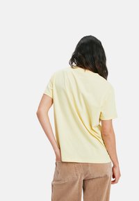 Gelbes T-Shirt mit kurzen Ärmeln, lockerer Passform und Rundhals, aus weicher Baumwolle gefertigt. Sichtbare Naht auf der Rückseite mit einem leicht längeren Saum.