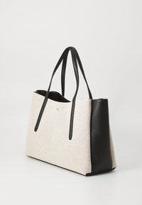 Beige lerret tote bag med svarte skinnaksenter og lange stropper. Rektangulær form med et minimalistisk design og subtil merking på forsiden.