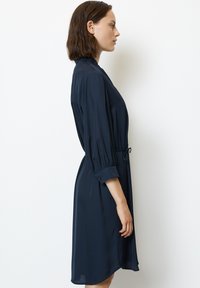 Abito blu navy in tessuto leggero, dotato di collo con revers, maniche a tre quarti e una cintura in vita regolabile per una forma aderente.