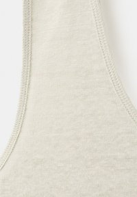 Gros plan sur un tissu tricoté beige clair montrant la couture incurvée du bord d’un vêtement sans manches.