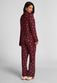 Bordeaux pyjama set met lange mouwen en broek, voorzien van een wit patroon van kleine figuren, zachte stof en een ontspannen pasvorm.