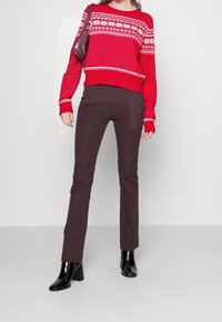 Pull en tricot rouge avec motif flocon de neige blanc, pantalon ajusté marron et bottes à talons noires. Le pull a un ourlet et des poignets côtelés.