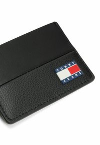 Portafoglio in pelle nera con finitura testurizzata. Presenta un logo Tommy Jeans multicolore in rosso, bianco e blu sulla parte anteriore.