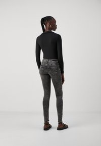 Body de manga larga negro combinado con jeans ajustados de talle alto en gris deslavado. El modelo completa el look con sandalias planas negras.