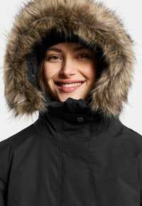 Zwarte parka met een door bont gevoerde capuchon. De capuchon heeft een dikke nepbont rand. De stof is glad, waarschijnlijk geïsoleerd voor warmte.